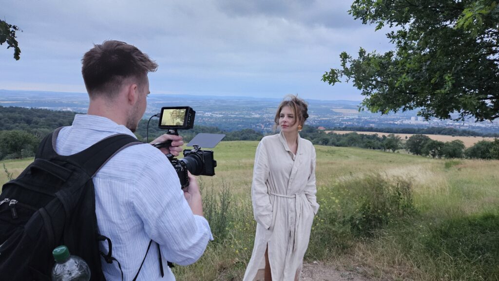 Kameramann filmt eine Frau im langen Mantel vor weiter Landschaft mit Blick auf das Tal