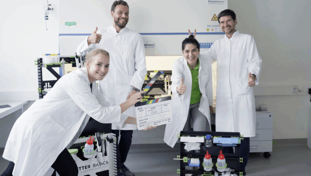 Team in Laborkitteln mit Filmklappe bei der Produktion eines Unternehmensvideos für Better Basics